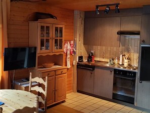 A compact kitchen with wooden cabinets, a built-in oven, and a dining area with a table and chairs. - David 26D, (Grächen), 1623 by Interhome (Grächen)