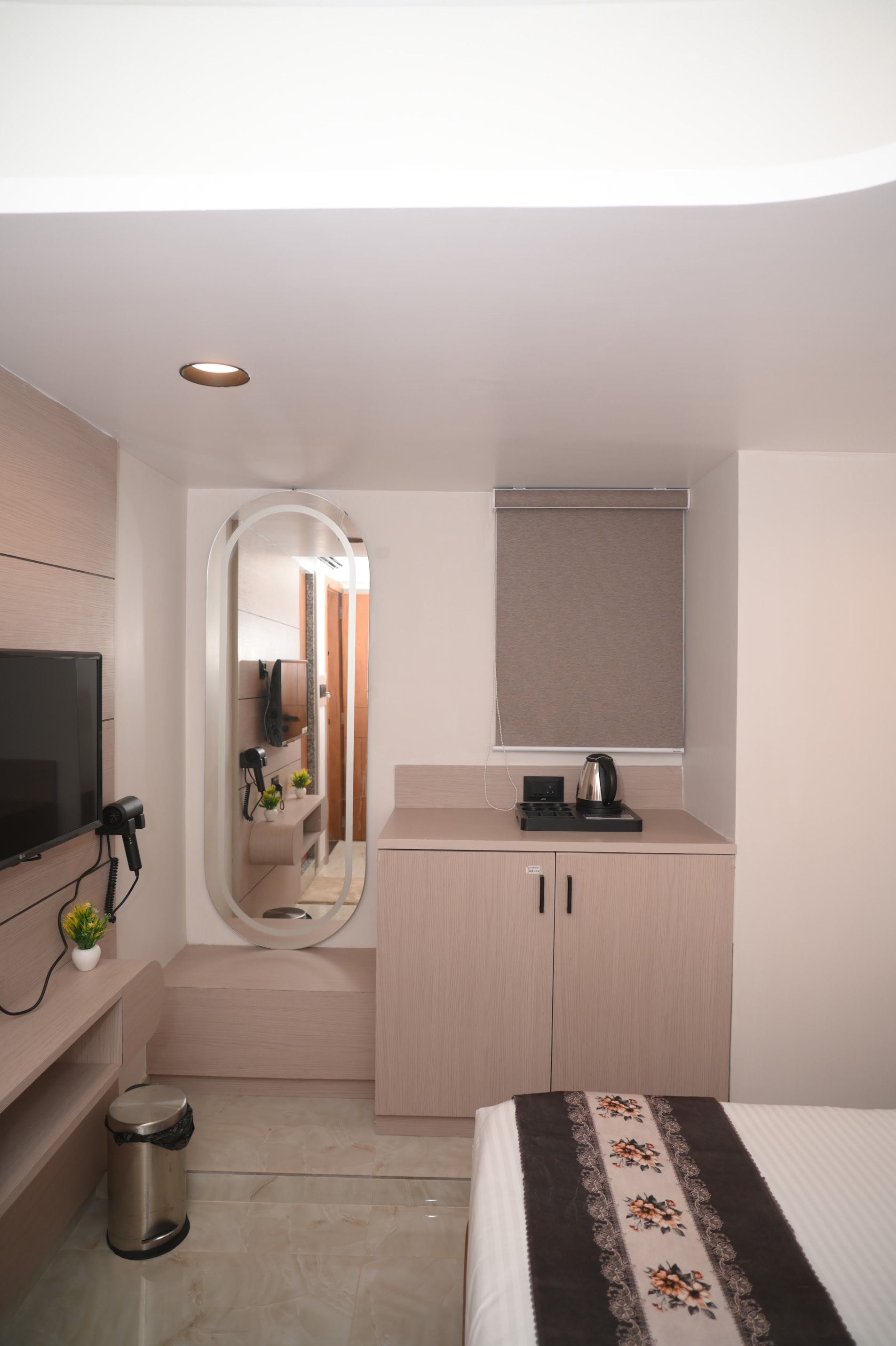 Een hotelkamer met een bed, een televisie, een spiegel, een kleine kitchenette en een prullenbak.