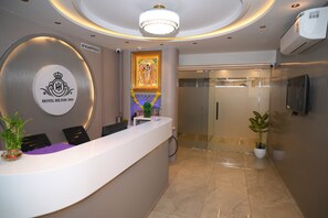 A hotel reception area with a modern design, including a reception desk, a framed religious painting, and a glass door leading to a hallway.