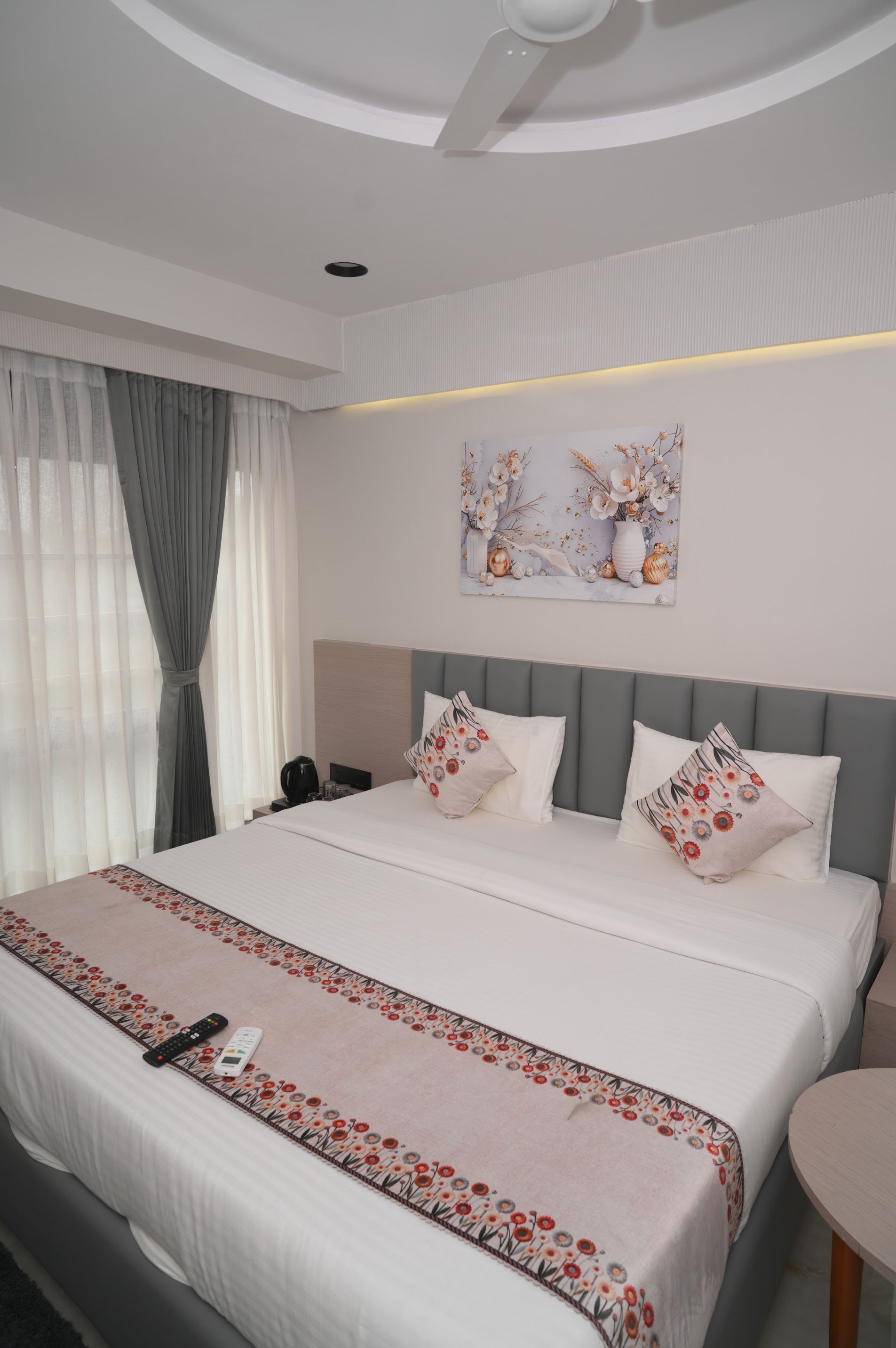 Habitación de hotel con una cama grande, una mesita de noche, una obra de arte colgada en la pared y un ventilador de techo.