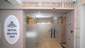 The entrance to Hotel Hilton Inn with a clear view of the reception area and a logo on the glass door.