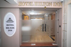 The entrance to Hotel Hilton Inn with a clear view of the reception area and a logo on the glass door.