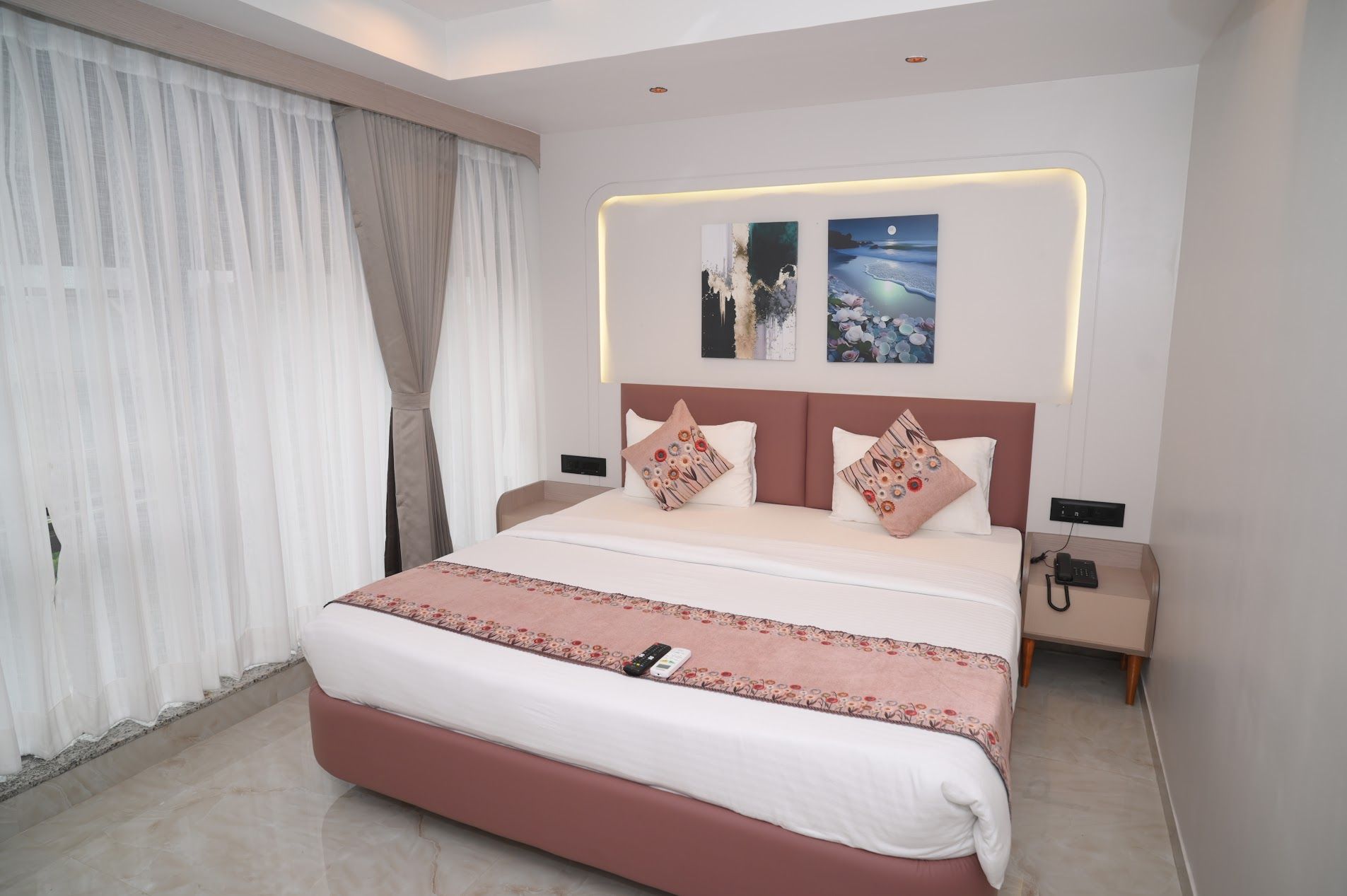 A modern hotel room with a large bed, a bedside table, a nightstand, and a wall-mounted artwork.