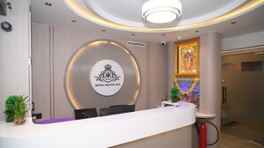 A hotel reception desk with a circular logo, a framed religious painting, and a fire extinguisher.
