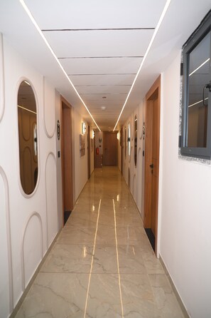 A hotel corridor with a marble floor, wooden doors, and illuminated ceiling lights.