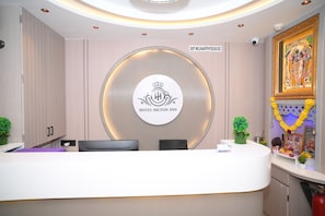Un mostrador de recepción de hotel con un logo circular, una cámara de seguridad y una pared decorativa con un cuadro enmarcado.