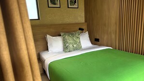 Una cama bien hecha con colcha verde y dos almohadas, una con diseño de hojas, en una habitación con paneles de madera y cuadros con motivos vegetales en la pared.