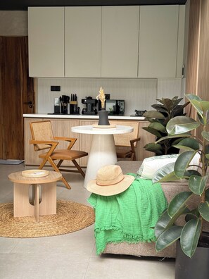 Una cocina moderna con armarios blancos, una zona de comedor con una mesa redonda y sillas, y una planta verde al frente.