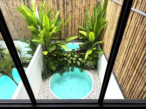Un espacio al aire libre pequeño y cercado, con una piscina rodeada de plantas y una valla de bambú.