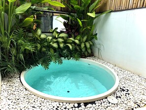 Ein runder Pool, umgeben von weißen Kieselsteinen und verschiedenen Grünpflanzen.