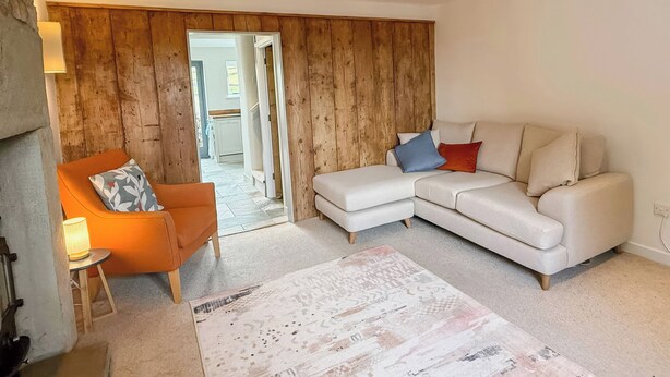 A living room with a sofa, a chair, a rug, and wooden paneling on the walls. - PEAK DREAMS, family friendly, character holiday cottage in Tideswell (Buxton)