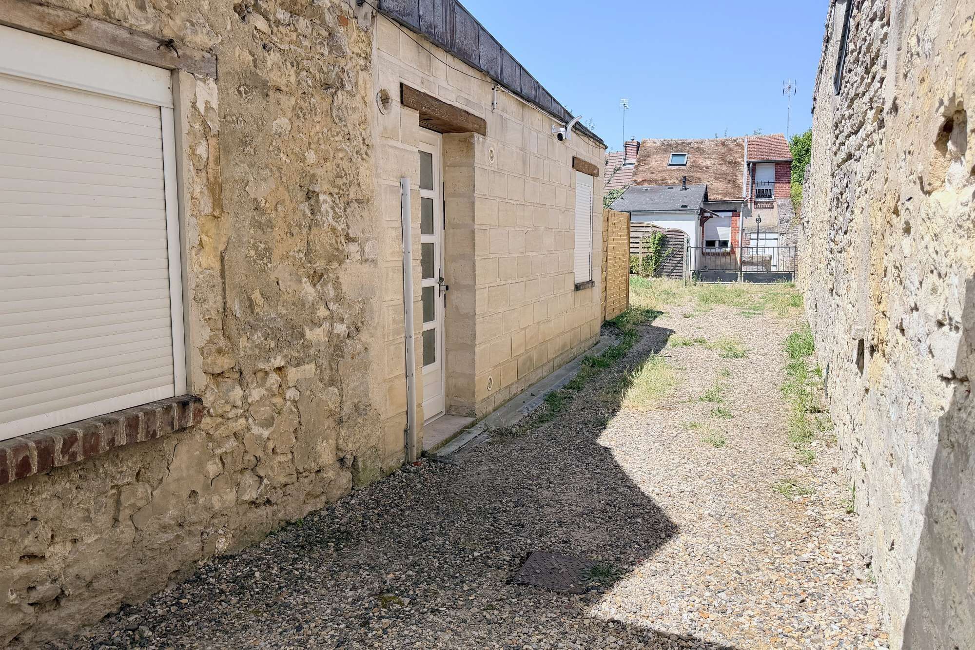 A narrow alley with a gravel path, a closed garage door, and a brick building with a door.