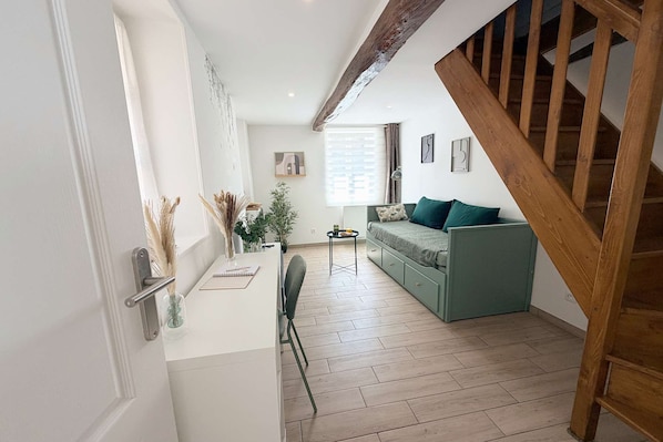 A modern living space with a wooden staircase, a green sofa, a small table with a notebook, and a potted plant. - La Green par Your Sweet Loc (Compiègne)