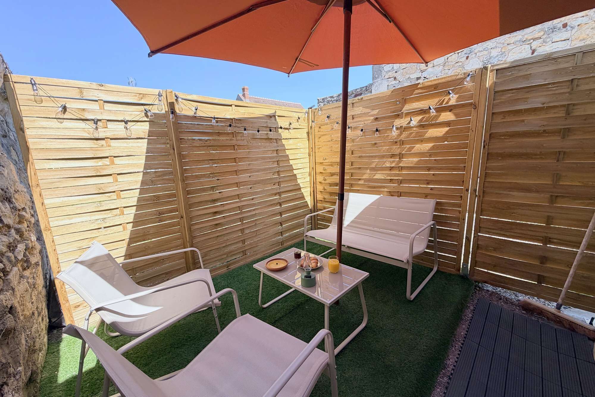 A patio with wooden slatted walls, a table with chairs, and an umbrella.