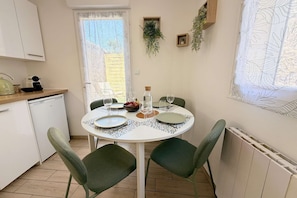A dining area with a round table, chairs, and a view of the outdoors through a window with a leaf-patterned curtain. - La Green par Your Sweet Loc (Compiègne)