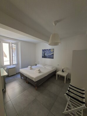 Ein Schlafzimmer mit einem Bett, einem Heizkörper, einem Fenster, einem Gemälde, einem Nachttisch und einer Hängeleuchte.