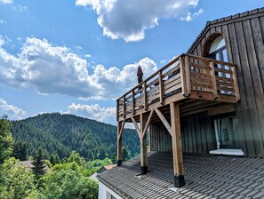 Un balcone in legno con vista su una catena montuosa boscosa.
