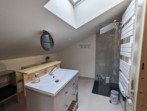 Un bagno moderno con una finestra a lucernario, un ampio specchio, un mobile bagno in legno e una cabina doccia in vetro.