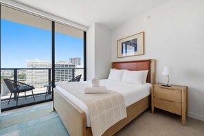 A hotel room with a large bed, a bedside table with a lamp, a chair, and a view of the city through a balcony. - The Crosby Balcony Studio Miami Worldcenter (Miami)