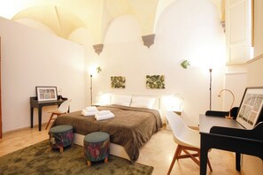 Ein Schlafzimmer mit Bett, Nachttischen, Schreibtisch, Stuhl und einem kleinen Hocker.