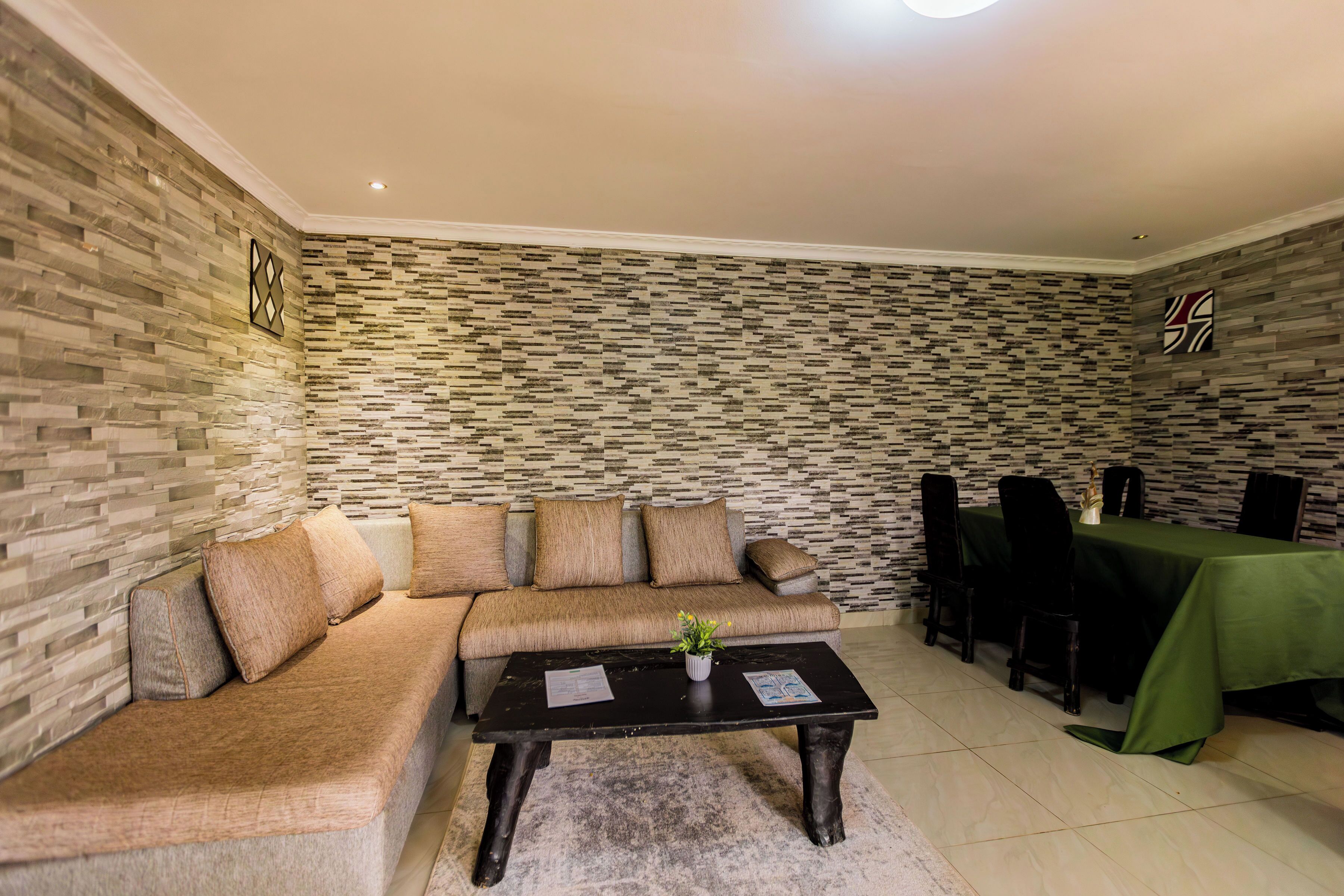 A room with a sectional sofa, a coffee table, a dining table with chairs, and a patterned wall.