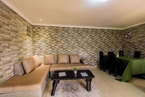 A room with a sectional sofa, a coffee table, a dining table with chairs, and a patterned wall. - The Green Resort (55VH+7R6, Kigali,)