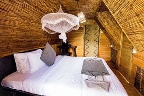 A room with a bed, pillows, a hanging mosquito net, and a small table.