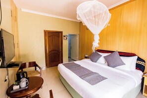 A hotel room with a bed, a television, a desk with a chair, and a nightstand. - The Green Resort (55VH+7R6, Kigali,)