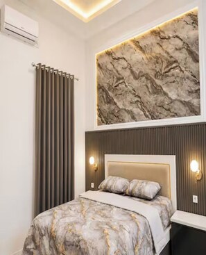 Ein Schlafzimmer mit einem Bett, einem Kopfteil, Wandleuchten, einer Heizung und einer großen, strukturierten Wand über dem Bett.