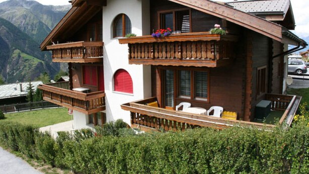 Ein Chalet mit Balkon, rotem Fensterladen und Bergblick.