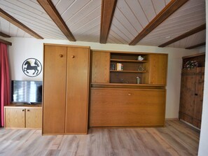Ein Zimmer mit Holzschrank, Fernseher und Holzgarderobe.