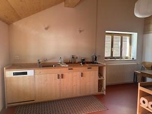 Una cocina con armarios de madera, lavavajillas, fregadero y ventana con persianas.