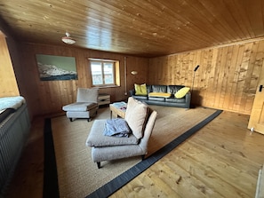 En mysig stuga med träpanel i taket, en soffa, en fåtölj, ett litet bord och ett fönster.