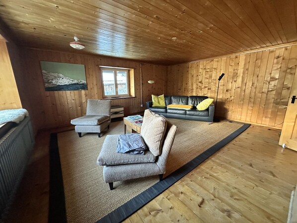 A cozy cabin interior with a wooden ceiling, a sofa, a chair, a small table, and a window.