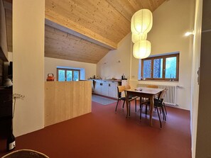 A modern kitchen with wooden beams, a dining area with a table and chairs, and large windows providing natural light.