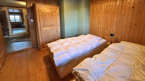 A wooden-paneled room with a bed, a wardrobe, and a door leading to another room.