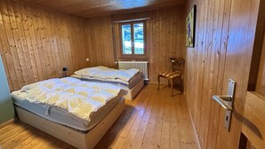Ein Schlafzimmer einer Holzhütte mit zwei Betten, einem Heizkörper, einem Fenster und einem Sessel.