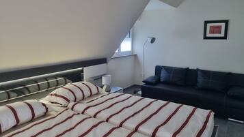 Ein modernes Schlafzimmer mit einem Bett, einem Sofa, einer Lampe und einem gerahmten Bild an der Wand.