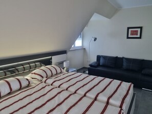 A modern bedroom with a bed, a sofa, a lamp, and a framed picture on the wall.