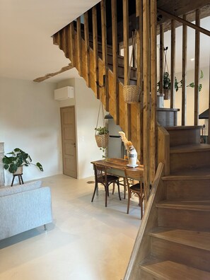 A wooden staircase with a rustic design, a dining area with a table and chairs, and a potted plant on a small stand. - Le Clos des Murmures - maisonnette mitoyenne à Trept (Trept)