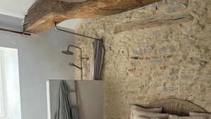 A bedroom with a stone wall, a bed with a white bedspread, and a wooden ceiling beam. - Le Clos des Murmures - maisonnette mitoyenne à Trept (Trept)