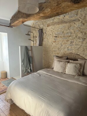 A bedroom with a stone wall, a bed with a white bedspread, and a wooden ceiling beam. - Le Clos des Murmures - maisonnette mitoyenne à Trept (Trept)