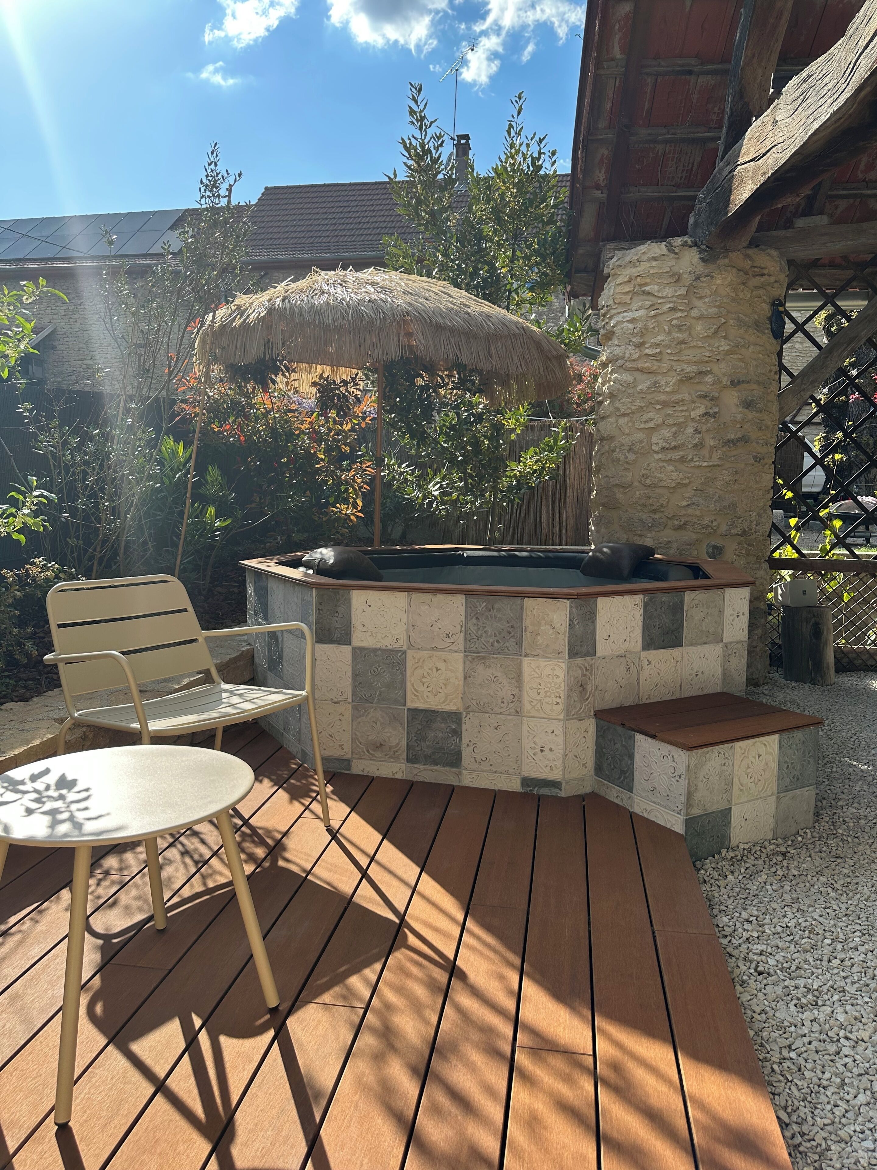 Une terrasse extérieure avec un mur en pierre, une table en bois, une chaise en métal et un parasol en chaume.