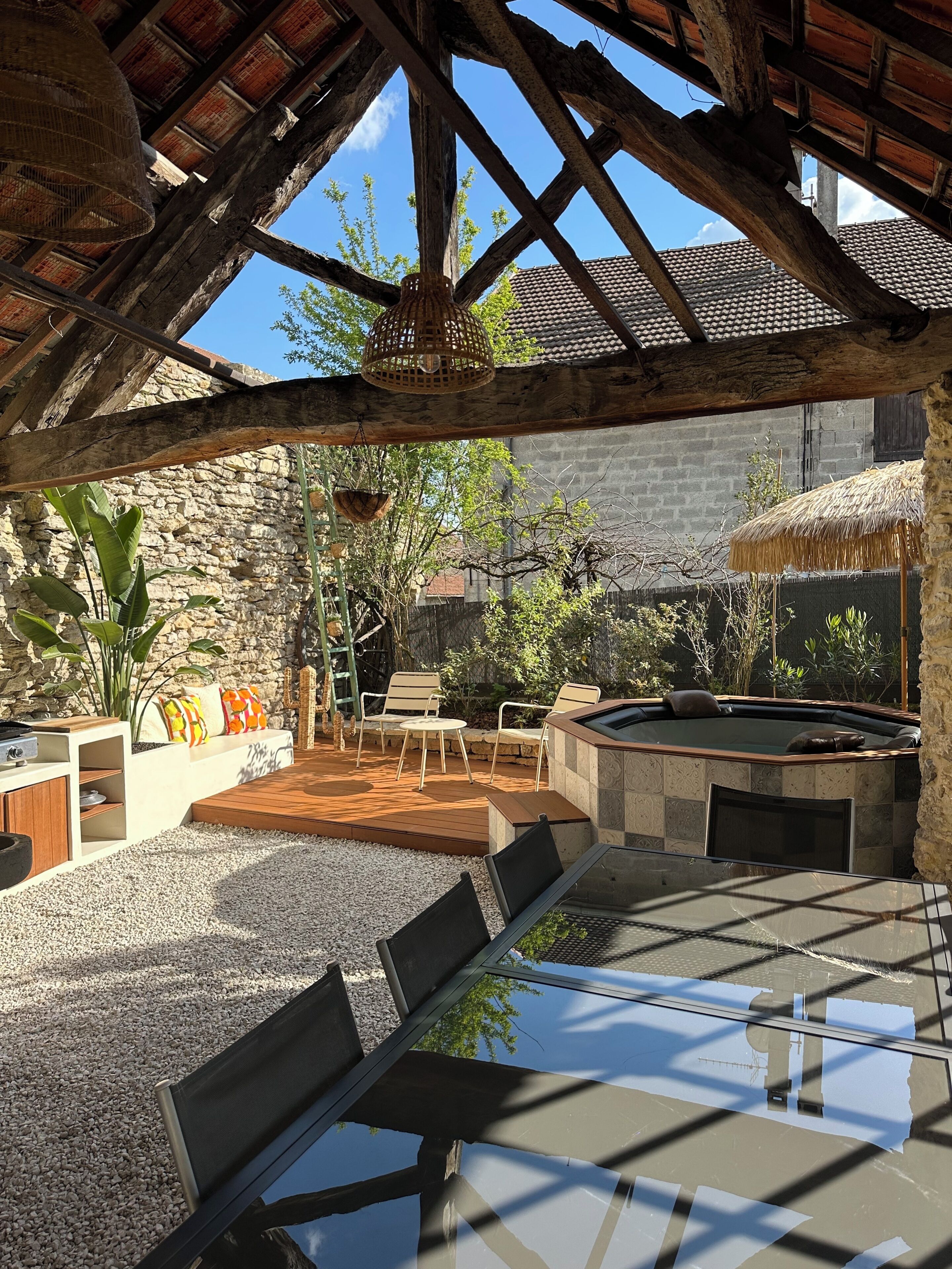 Une terrasse extérieure avec une table en verre, des chaises et un jacuzzi.