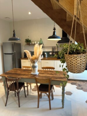 A dining area with a wooden table, chairs, hanging baskets, and pendant lights. - Le Clos des Murmures - maisonnette mitoyenne à Trept (Trept)