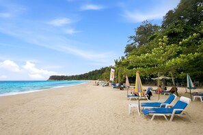 Ein Strand mit Liegestühlen und Sonnenschirmen, einem wolkenlosen Himmel und ruhiger See.