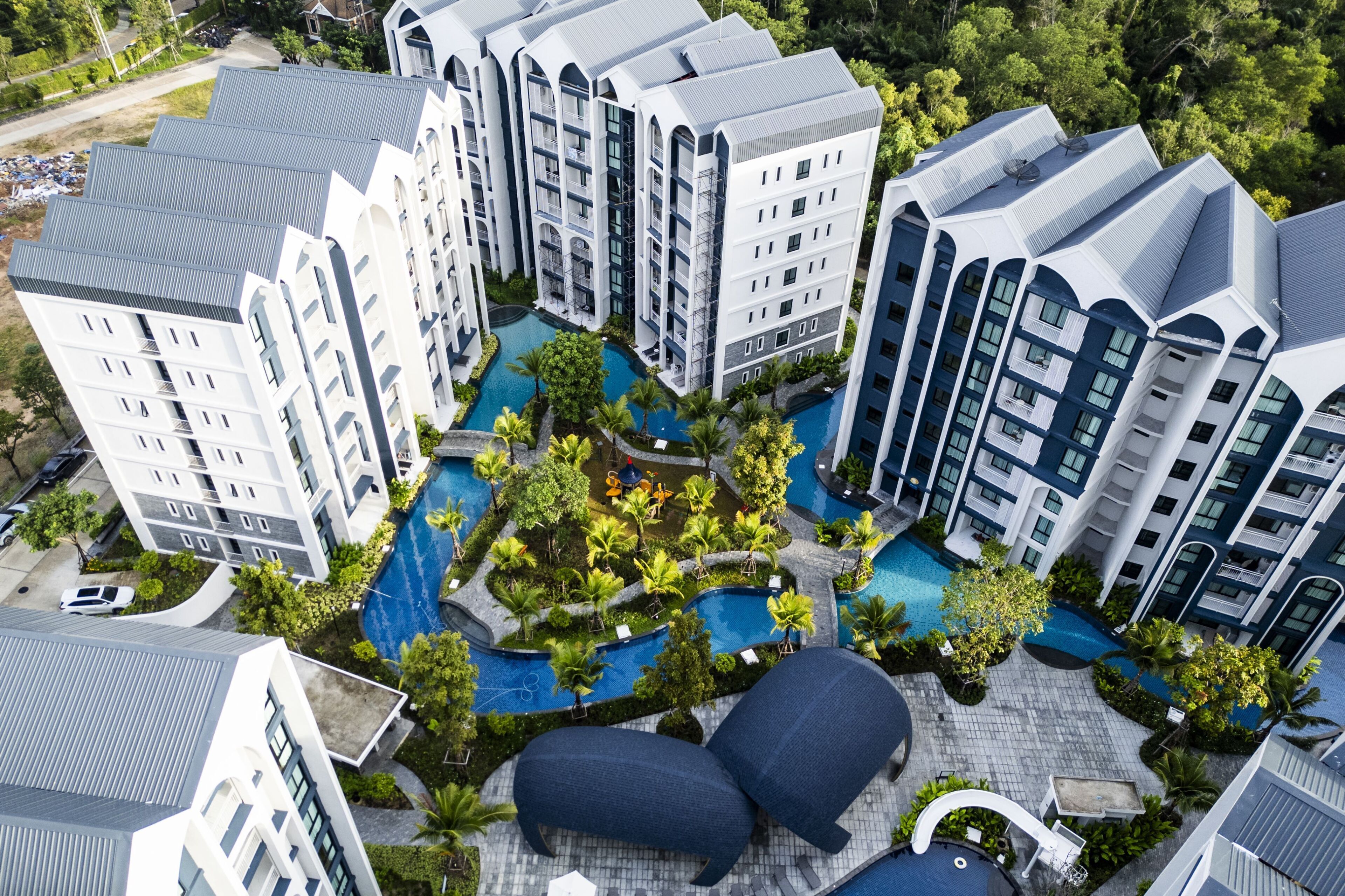 A high-rise residential building with multiple balconies, a central swimming pool, and surrounding greenery.