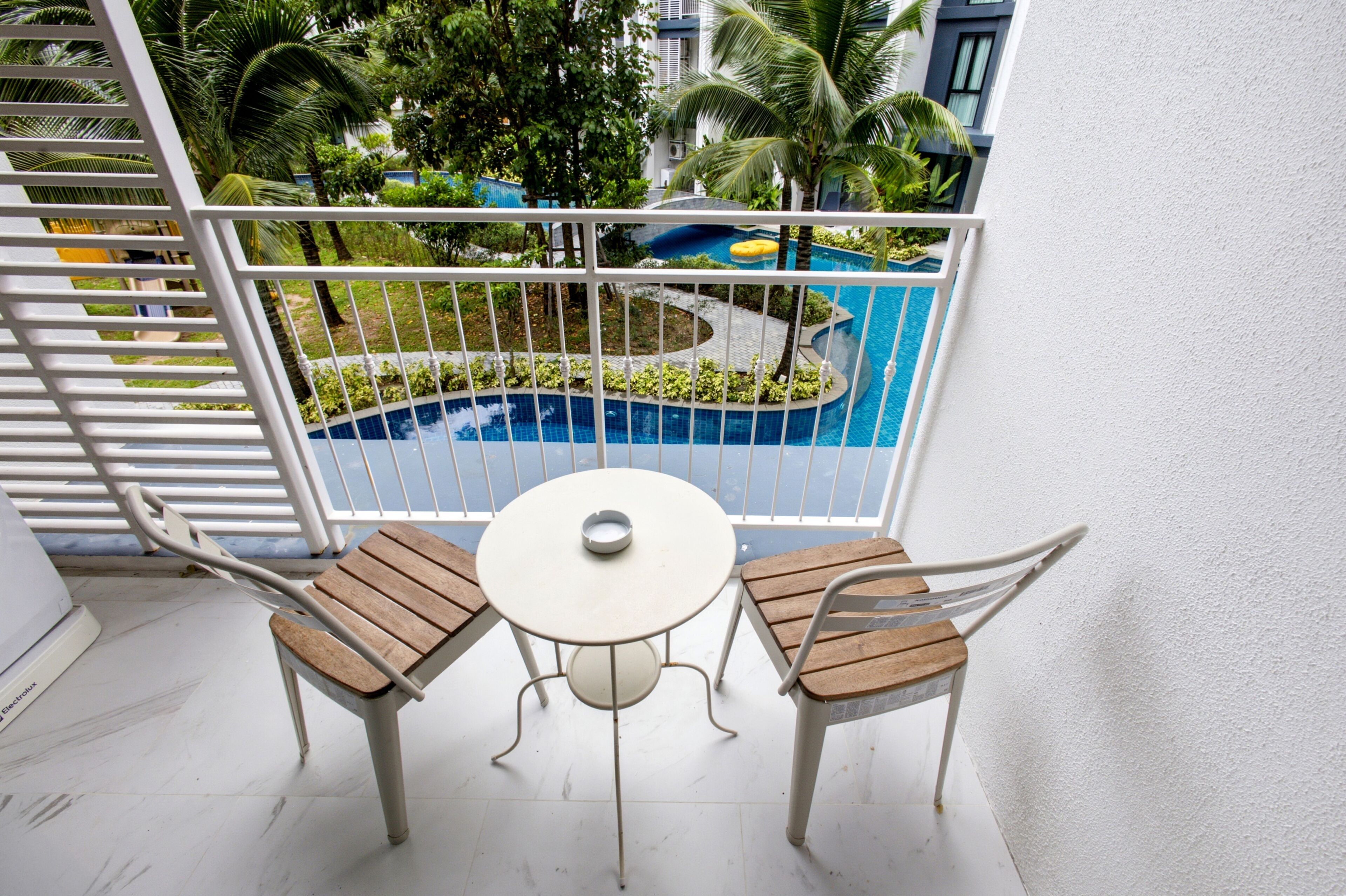 Ein Balkon mit weißer Brüstung, zwei Holzstühlen und einem kleinen runden Tisch.