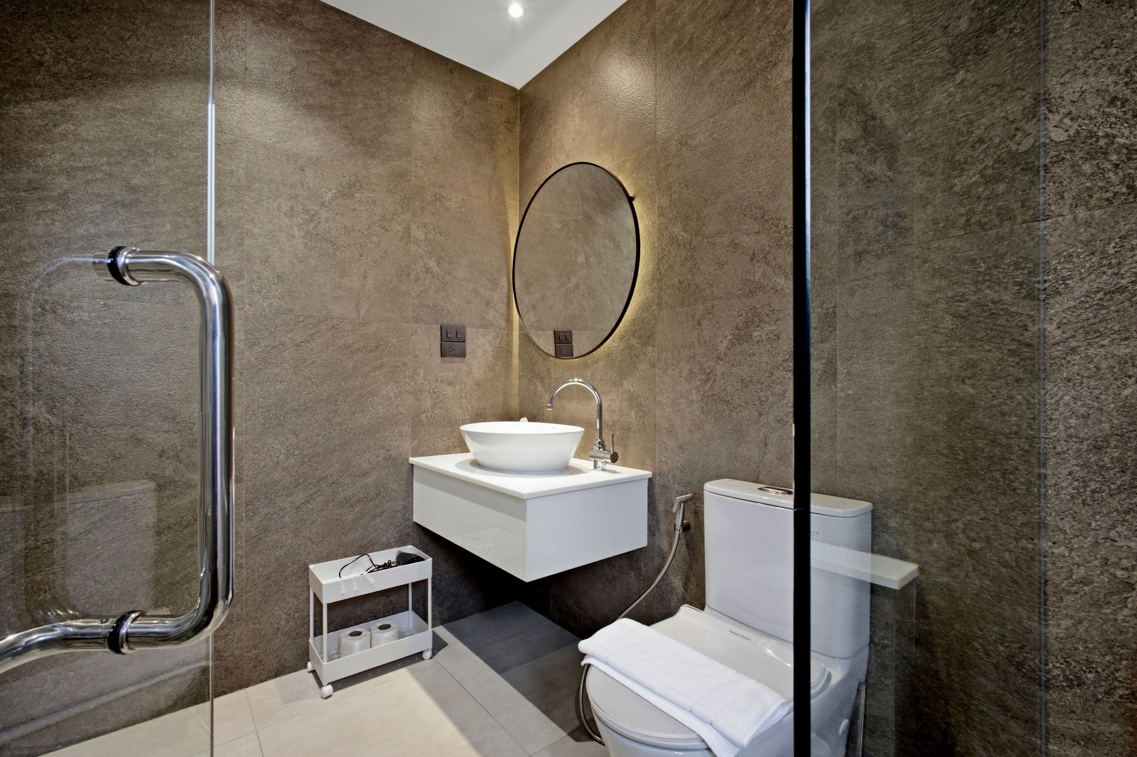 Une salle de bain moderne avec une douche à parois de verre, un lavabo blanc avec un miroir rond et des toilettes.