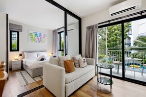 Ein modernes Hotelzimmer mit Bett, einer Sitzecke, einem kleinen Tisch und einem Balkon mit Blick auf Grünflächen und einen Pool.